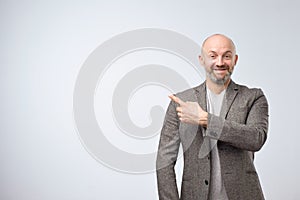 Portrait of a happy businessman in casual suit pointing finger away over white background