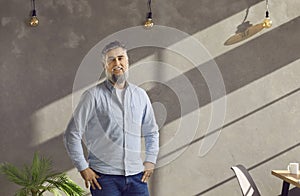 Portrait of a happy mature businessman standing in the office against a grey wall