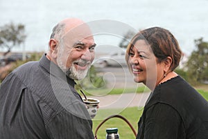 portrait of a happy mature couple laughing and drinking yerba mate outdoors