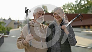 Portrait of the happy mature family standing in the park after scandinavian walking holding the trekking poles. Elderly