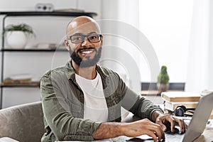 Portrait of happy mature latin man sitting at desk, working on pc laptop and smiling at camera, free space