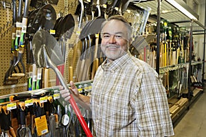 Portrait of a happy mature man holding shovel in hardware store