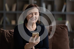 Portrait of happy mature 60s woman holding mobile phone