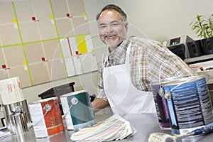 Portrait of a happy mature sales clerk at counter with paint cans in hardware store