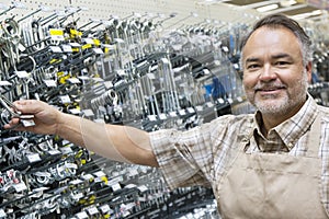 Portrait of a happy mature salesperson holding metallic equipment in hardware store