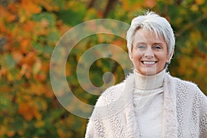 Portrait of a happy mature woman with warm pullover in nature