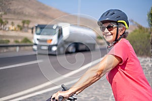 Portrait of happy mature woman, wearing protective helmet, on her bike in the sunny road. Healthy and active retirement concept