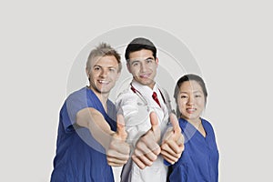 Portrait of a happy medical team gesturing thumbs up over gray background