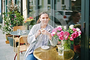 Portrait of happy middle age woman relaxing in outdoor cafe, holding cup of coffee