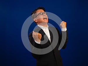 Portrait of happy middle-aged asian confident successful businessman wearing suit celebrating on blue background in studio,