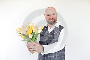 Portrait of happy middle-aged businessman in grey vest, white shirt holding, giving bouquet of yellow tulips. Holiday.