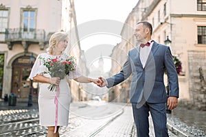 Portrait of happy middle aged couple in love, holding hands, having a date in ancient city