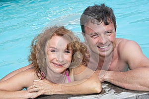 Portrait of happy middle aged couple relaxing on the edge of swimming pool