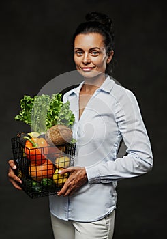 Portrait of a happy middle-aged woman in apron holds a basket of fresh vegetables and fruit