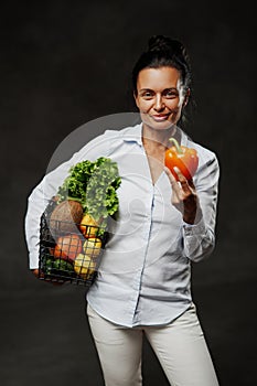 Portrait of a happy middle-aged woman in apron holds a basket of fresh vegetables and fruit