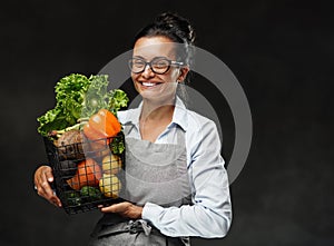 Portrait of a happy middle-aged woman in apron holds a basket of fresh vegetables and fruit