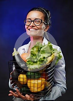 Portrait of a happy middle-aged woman in apron holds a basket of fresh vegetables and fruit