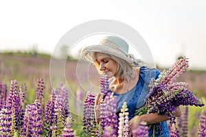 Portrait of happy middle-aged woman in hat on a flowering lupine field.