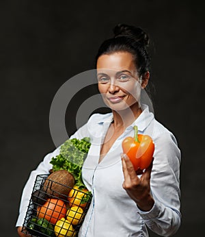 Portrait of a happy middle-aged woman holds a basket of fresh vegetables and fruit