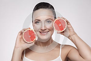 Portrait of happy middle aged woman with perfect skin smiling after cream, balm, mask, lotion, holding fresh slice grapefruit in
