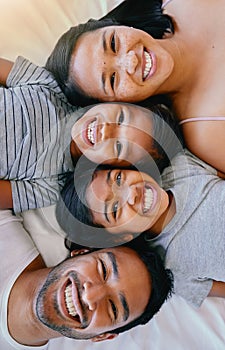 Portrait of a happy mixed race family of four in pyjamas lying cosy together in a row on a bed smiling and taking fun