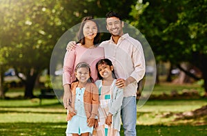 Portrait of a happy mixed race family standing together in a public park on a sunny day. Asian parents and two little