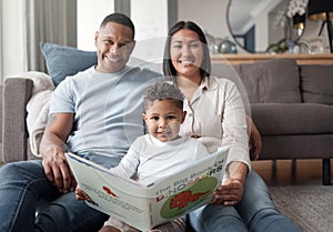 Portrait of a happy mixed race family of three relaxing on the lounge floor and reading a story book at home. Loving