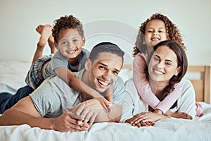 Portrait of happy mixed race family with two children lying on the bed at home. Smiling couple bonding with their son