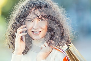 Portrait of a happy modern girl with dental braces and and curly hair.  Happy woman with shopping bags and smarphone