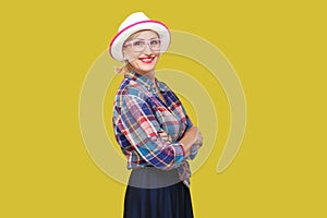 Portrait of happy modern stylish mature woman in casual style with hat and eyeglasses standing, crossed arms and looking at camera