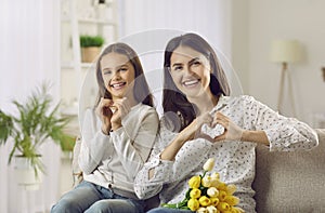 Portrait of happy mom and daughter together doing heart sign with hands on Mother& x27;s Day