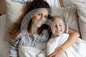 Portrait of happy mom and little daughter cuddle in bed