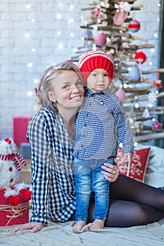 Portrait of happy mother and adorable baby celebrate Christmas. New Year`s holidays. Toddler with mom in the festively decorated r