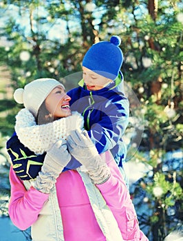 Portrait of happy mother and child son dressed in colorful sportswear together in winter park on christmas tree background