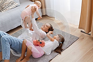 Portrait of happy mother and children playing in the living room resting on the floor, mommy raising arms and holding infant baby