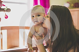 Portrait of a happy mother with cute baby in crib giving kiss