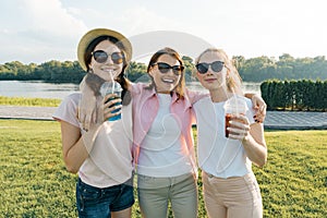 Portrait of happy mother and daughters teenagers 14 and 16 years old, girls with summer drinks. Background nature, recreation area