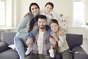 Portrait of happy mother, father and little children sitting on couch and smiling at camera