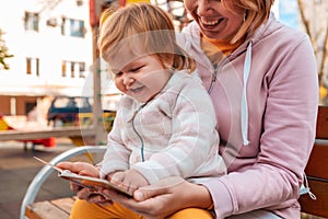 Portrait of a happy mother and her little daughter, reading a book together, sitting on a bench. The concept of child