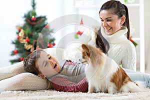 Portrait of a happy mother and her little son with dog spending together Christmas time at home near the x-mas tree