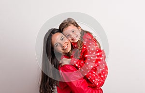 Portrait of a happy mother holding a small girl with red anorak in studio.