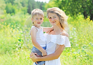 Portrait of happy mother hugging child son outdoors in summer