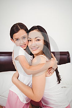 Portrait of happy mother hugging daughter on bed