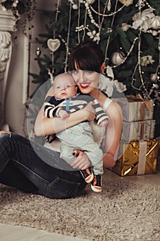 Portrait of happy mother and litle baby near decorated christmas tree with gifts.