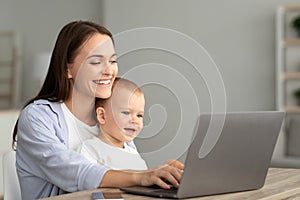 Portrait Of Happy Mother With Little Baby On Hands Using Laptop Together