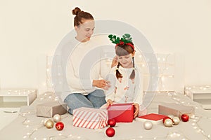 Portrait of happy mother and little daughter opening christmas gifts in bed at home, spending new year eve together, celebrating