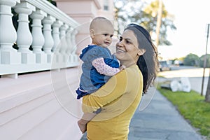 Beautiful happy mother holding her cute baby in peaceful neighborhood