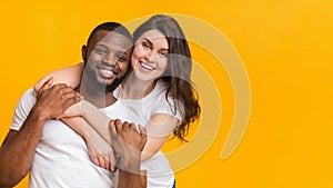 Portrait of happy multiracial couple embracing, posing together over yellow background