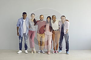 Portrait of happy multiracial friends standing embracing against the backdrop of a light wall.