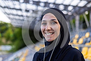 Portrait of happy muslim woman in hijab and headphones on court, doing sports and listening to music, smiling and